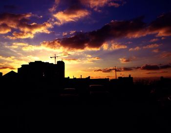 Silhouette of buildings against cloudy sky at sunset