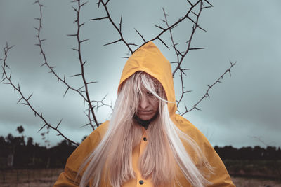 Girl in yellow raincoat cloudy rainy weather from behind tree branch with thorns mystic sign concept