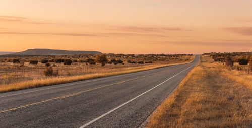 Road by landscape against sky during sunset