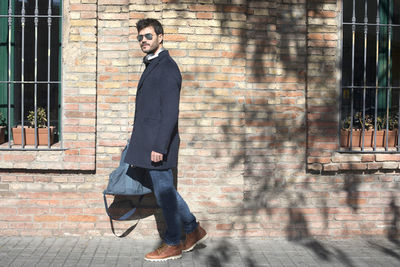 Portrait of man in sunglasses walking by brick wall