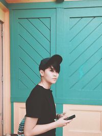 Young man using mobile phone against wall