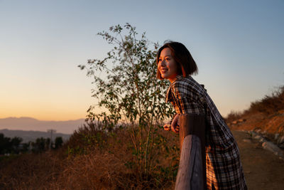 Side view of young woman standing on field against sky