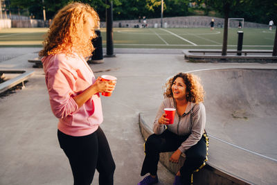 Smiling young women talking while having drinks at skateboard park