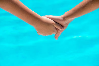 Cropped image of friends holding hands against turquoise swimming pool