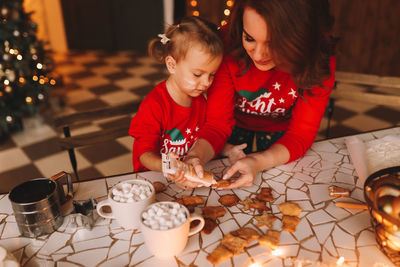 Happy parent and child in red pajamas prepare christmas cookies in the decorated kitchen of house