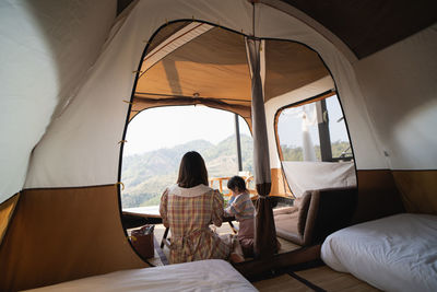 Rear view of mother and daughter sitting in tent