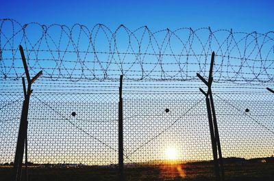 Barbed wire against clear sky seen through chainlink fence