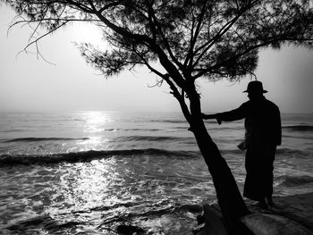 Silhouette man standing by sea against sky