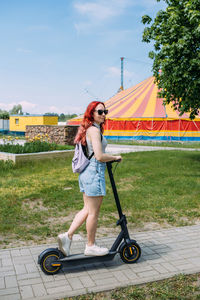 Young bright woman smiles and rides electric scooter in the summer in the city