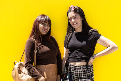 Portrait of smiling young women against yellow background