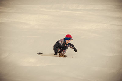 Smiling boy tobogganing on snow covered field during winter