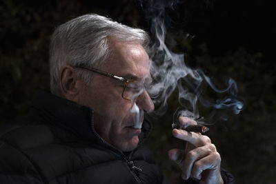 Senior man smoking cigar against black background