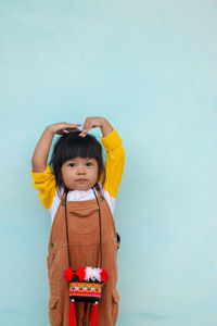 Cute baby girl with arms raised standing against wall