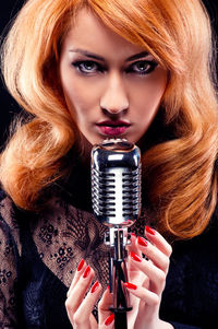 Close-up portrait of young woman with microphone against black background