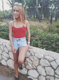 Portrait of young woman standing by retaining wall against trees