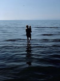 Rear view of mother carrying son while standing in sea