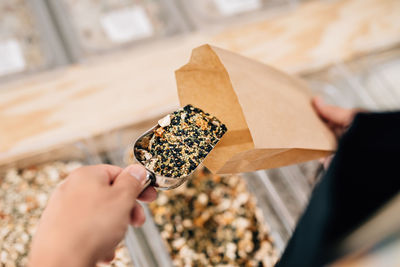 Top view of anonymous person pouring spices inside paper bag in local store