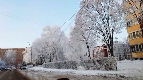 Snow covered road by buildings against sky