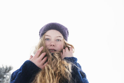 Low angle portrait of woman with blond hair standing against clear sky during winter