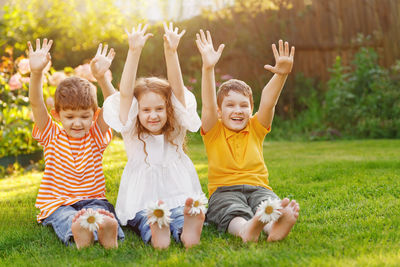 Happy friends children with daisy flowers at green grass in a summer park.