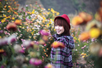 Side view portrait of smiling young woman standing amidst flowering plants on field