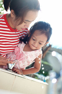 Low angle view of mother assisting daughter in drinking water through fountain