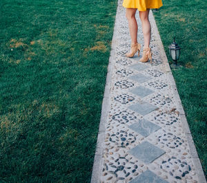 Low section of woman standing on walkway amidst grassy field