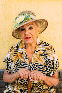 A very old woman in a hat with bright makeup near her house