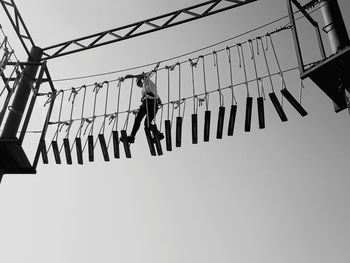 Low angle view of woman walking on rope footbridge against sky