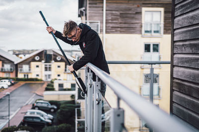 Side view of young man holding umbrella against building in city