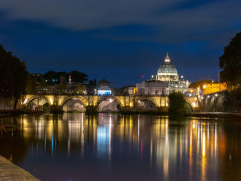 Illuminated arch bridge over river against sky in city