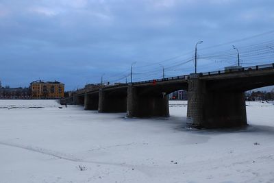 Bridge over snow covered land against sky