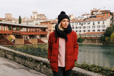 Portrait of young woman standing against building in city