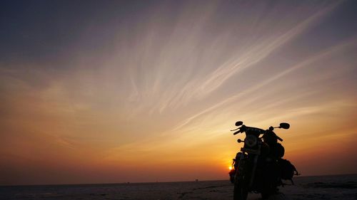 Silhouette of motorcycle on beach at sunset