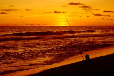 Silhouette man fishing in sea against orange sky