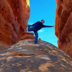 Low angle view of man practicing yoga on rock formation against sky