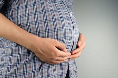 Midsection of woman touching tree against gray background