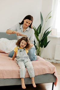 Portrait of smiling mother and daughter sitting on sofa at home