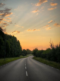 Road by trees against sky during sunset