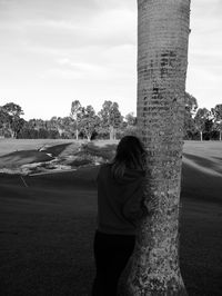 Rear view of woman standing by tree on field against sky