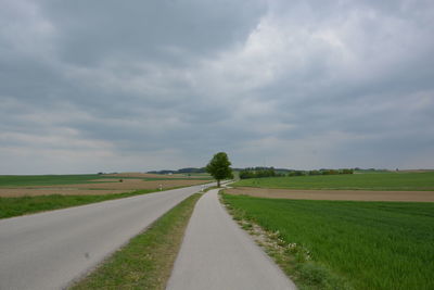 Empty road amidst field against sky