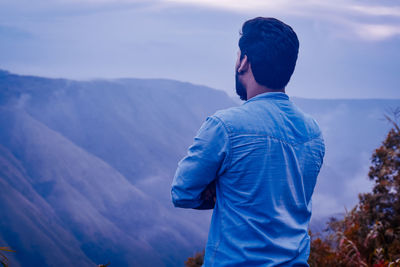 Rear view of man looking at mountains against sky