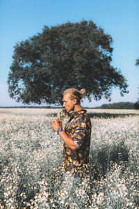 Man smelling flowers while standing against tree