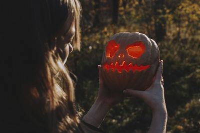 Young woman looking at jack o' lantern while standing in forest during halloween