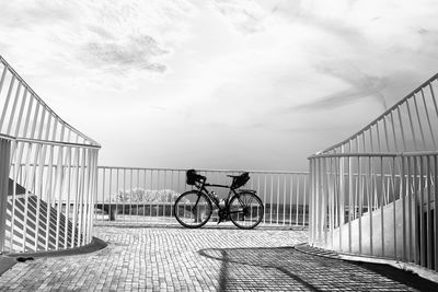 Bicycle on railing by bridge against sky