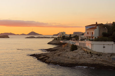 Buildings by sea against sky during sunset