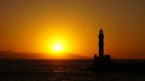 Silhouette lighthouse by sea against orange sky