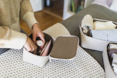 Hands of woman packing beauty product in pouch on bed