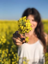 Young woman holding yellow flowers at oilseed rape field