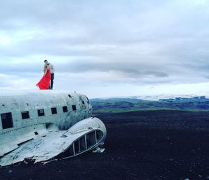 People standing on abandoned car against sky